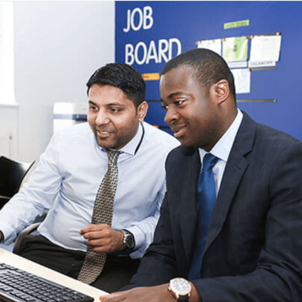 Two men using computer in-front of a job board