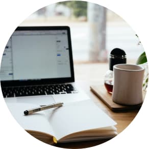 Laptop on desk with a notebook and pen